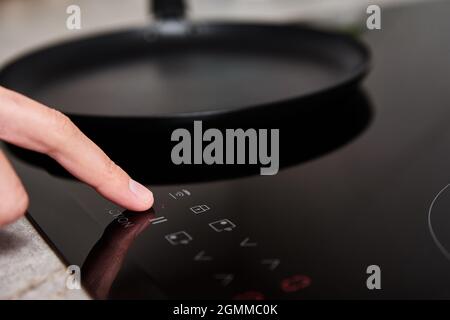 Modern kitchen appliance. Woman hand turn on induction stove to cook. Finger touching sensor button on induction or electrical hob Stock Photo