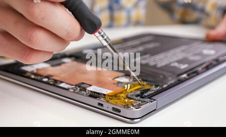 Unrecognizable man disassembles a laptop and looks through the parts with a screwdriver Stock Photo