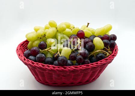 Fresh Red and White Grapes in a red basket isolated on white background. Stock Photo
