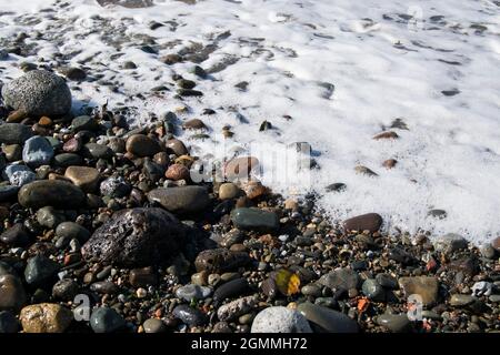 White water foam lapping on the pebble shore at Maryport in Cumbria Stock Photo