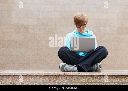 Modern wireless technology concept - woman with short hair with a laptop in an urban environment. She works intently, sitting on the parapet against t Stock Photo