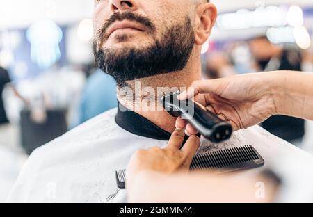 Hands grooming the beard of a man with an electric razor in a barber shop Stock Photo