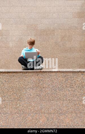 Vertical photo. Modern wireless technology concept - woman with short hair with a laptop in an urban environment. She works intently, sitting on the p Stock Photo