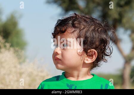 close-up profile view portrait of A small cute Indian Hindu child wearing a green shirt stands outside looking away Stock Photo