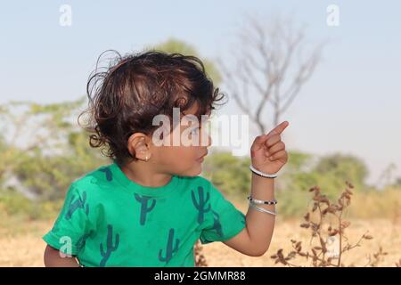 Close-up profile view portrait of A small cute Indian Hindu child wearing a green shirt stands outside, showing a distant object with a finger gesture Stock Photo