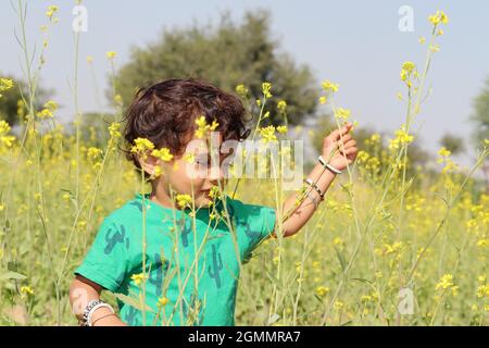 Close-up portrait of A beautiful cute Indian Hindu little child enjoying and playing in a mustard field wearing a green shirt Stock Photo