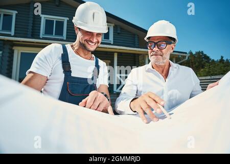Joyful engineer looking at drawings location, pointed out by colleague Stock Photo