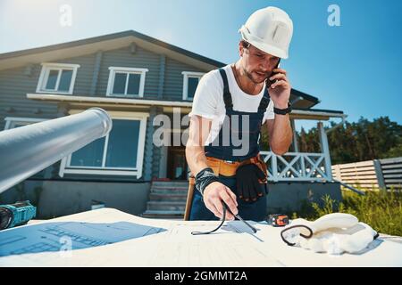 Man picking up walkie talkie from table while using phone Stock Photo