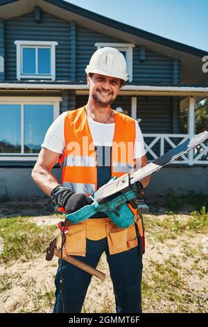 Happy construction worker standing with chainsaw in hands Stock Photo