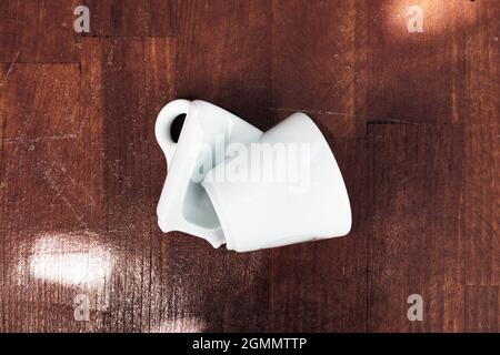 Broken white espresso coffee cup on wooden table. Stock Photo