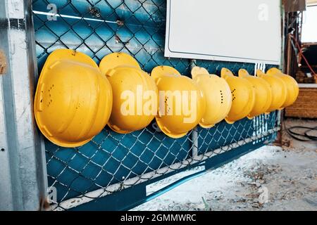 Yellow safety hats hanging on a wire fence in a row at the construction site. Work safety. Stock Photo