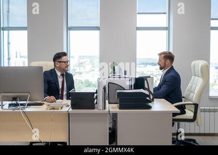 Two confident businessmen sitting in front of computer monitors while working in office Stock Photo