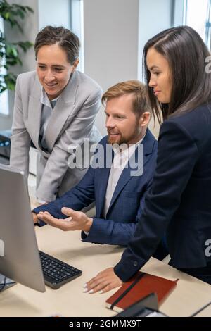 Three young office workers in suits looking at computer screen during presentation Stock Photo