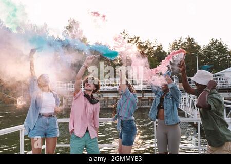 Cheerful young people in casualwear dancing with firecrackers by waterside on summer day Stock Photo