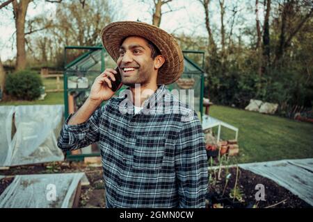 Mixed race male farmer standing outdoors talking on cellphone Stock Photo