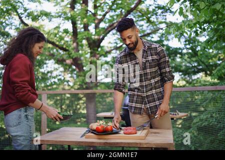 Happy couple resting and preparing burgers outdoors in a tree house, weekend away and digital detox concept. Stock Photo