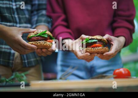 Close up of unrecognizable couple holding burgers outdoors in a tree house, weekend away and digital detox concept. Stock Photo