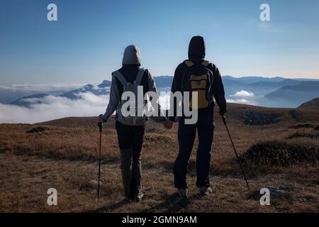 Hiking adventure healthy outdoors people standing talking. Couple enjoying view above clouds on trek. young woman and man in nature wearing hiking bac Stock Photo