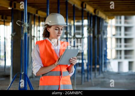 Female construction engineer. Architect with a tablet computer at a construction site. Young Woman looking, building site place on background. Construction concept. Stock Photo