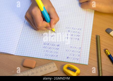 Close-up pupil's hand writes with a ballpoint pen in a notebook. A schoolboy performs a task at the workplace. The concept of children's education, teaching knowledge, skills and abilities. Stock Photo