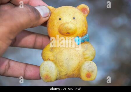 Selective focus on yellow teddy bear in human hand isolated with blur background in the park in the morning sunlight in INDIA. Plastic teddy bear. Stock Photo