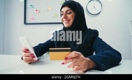 Muslim businesswoman smiling while using smartphone and credit card Stock Photo