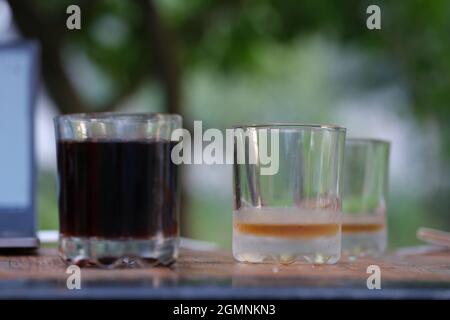 Two transparent glass glasses full of dark liquid and empty stand on table Stock Photo