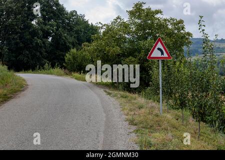 Left bend in a road, with a warning sign for a sharp left turn Stock Photo