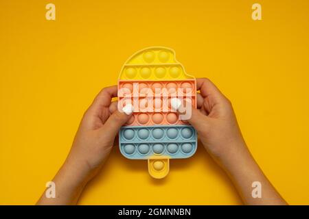 Child's hand presses on pop it toy silicone on a yellow background Stock Photo