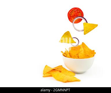 Nachos with vegetables in a white plate. Uncut onion rings and tomato flying into a plate. Copy space. Stock Photo