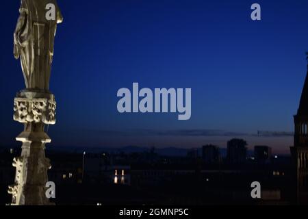 Sunset in background from rooftop of Duomo Di Milano with statue to the left Stock Photo