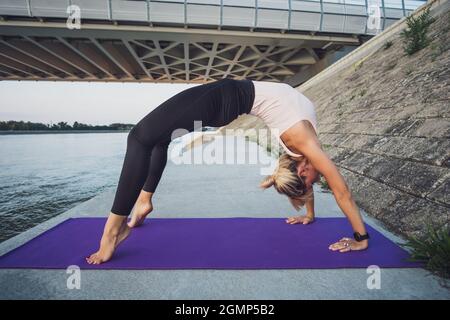 Young woman is exercising outdoor. She is practicing yoga. Urdhva Dhanurasana / Bridge pose. Stock Photo