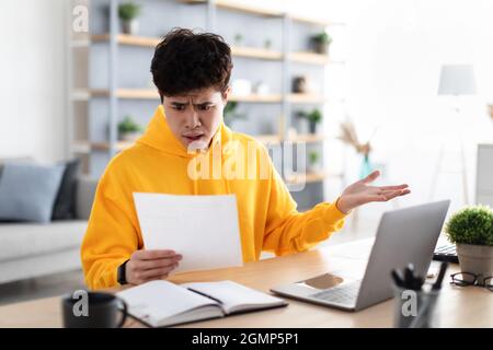 Confused asian man holding paper reading report working on laptop Stock Photo