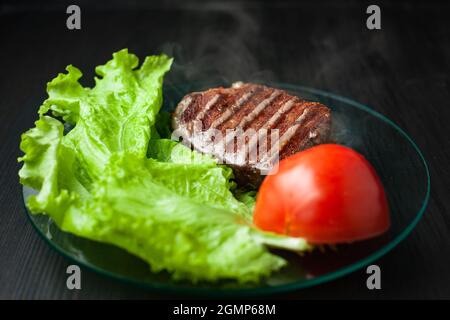 Hot piece of roasted meat on a plate with vegetables on a dark background Stock Photo