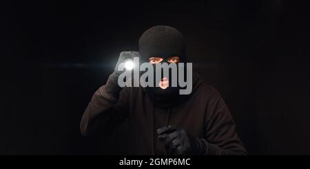 Masked burglar with flashlight on dark back Stock Photo
