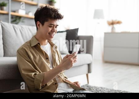 Closeup of smiling asian man using smartphone at home Stock Photo