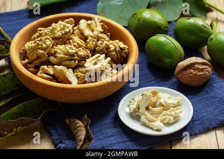 Young walnuts, shelled and in shell, walnut leaves. Rustic style. Stock Photo