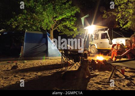 Black African family sitting around the campfire with their dog in the outback on a camping trip at a campsite at Beaverlac, Porterville. South Africa Stock Photo