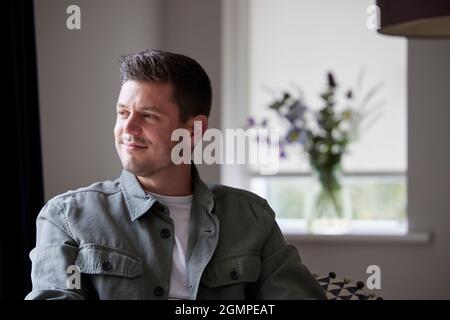 Thoughtful And Content Man Sitting On Chair At Home Looking Out Of Window Stock Photo