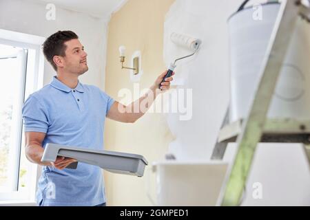 Man Painting Wall In Room Of House With Paint Roller Stock Photo
