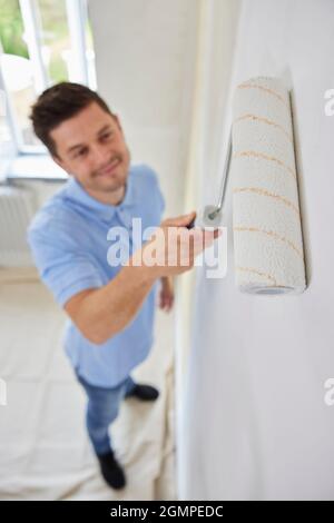Man Painting Wall In Room Of House With Paint Roller Stock Photo