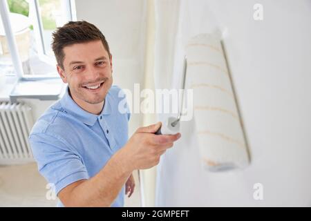 Portrait Of Man Painting Wall In Room Of House With Paint Roller Stock Photo