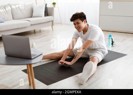 Asian guy doing stretching exercise using laptop Stock Photo