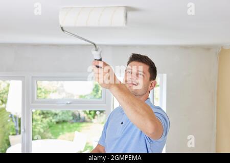 Man Painting Ceiling In Room Of House With Paint Roller Stock Photo