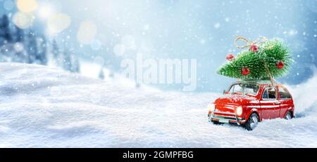 Retro toy car carrying christmas tree on a roof in snowy winter forest. Christmas background. Stock Photo
