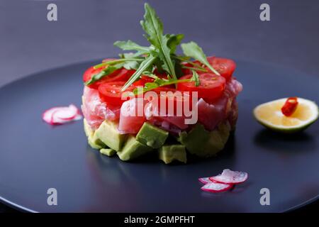 Fresh tuna tartare with avocado, arugula, cherry tomatoes, radish, chili and lime. Traditional cold appetizer of French cuisine. Close-up. Stock Photo
