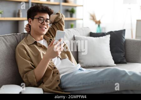 Smiling asian man in glasses using smartphone at home Stock Photo