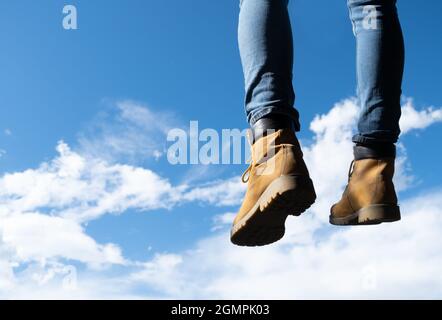 Hanging feet with mountain boots, sky in the background, beautiful nature scenario Stock Photo