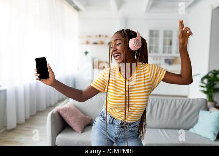 Joyful afro american long-haired woman singing and dancing, using smartphone Stock Photo