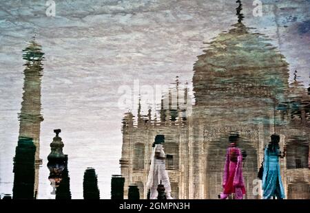 Three women wearing colorful saris are reflected in the pool in front of the Taj Mahal. Agra, Uttar Pradesh, India. Stock Photo
